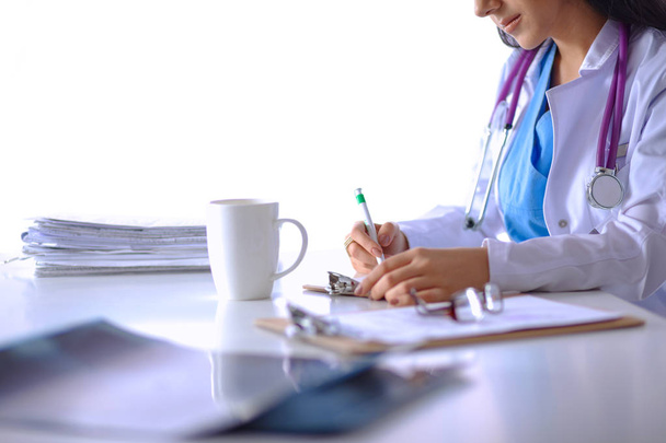Όμορφη νεαρή χαμογελαστή γυναίκα γιατρός κάθεται στο γραφείο - Φωτογραφία, εικόνα