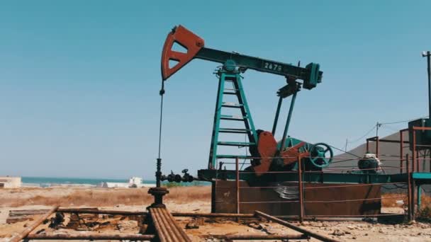 Sziluettjét olajszivattyú és egy régi rozsdás vas hordó közelében a háttér a kék ég és a felhők. Olaj pumpjacks működő olaj mezőben lévő Baku, Azerbajdzsán. - Felvétel, videó