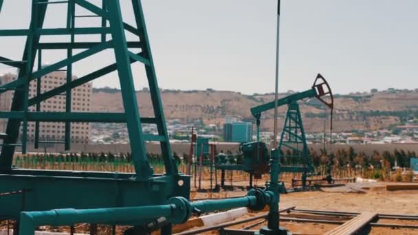 Część pumpjacks oleju w polu pracy ropy w Baku, Azerbaijan.Silhouette pracy pompy oleju i starej beczki zardzewiały żelazo w pobliżu na tle błękitnego nieba i chmur - Materiał filmowy, wideo