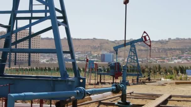 Część pumpjacks oleju w polu pracy ropy w Baku, Azerbaijan.Silhouette pracy pompy oleju i starej beczki zardzewiały żelazo w pobliżu na tle błękitnego nieba i chmur - Materiał filmowy, wideo