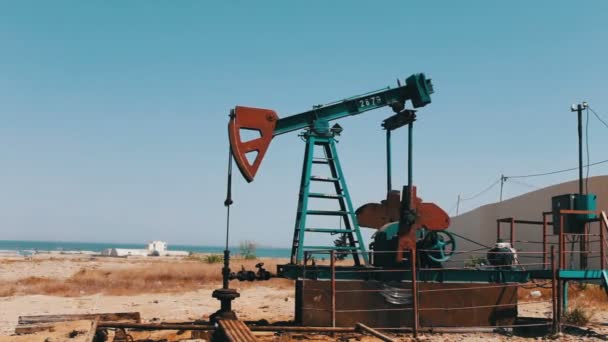 Silhouette of working oil pump and an old rusty iron barrel near on a background of blue sky and clouds.Oil pumpjacks in a working oil field in Baku, Azerbaijan. - Footage, Video