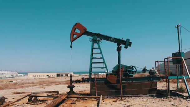 Working oil pump and an old rusty iron barrel near on a background of blue sky and clouds.Oil pumpjacks in a working oil field in Baku, Azerbaijan. - Footage, Video