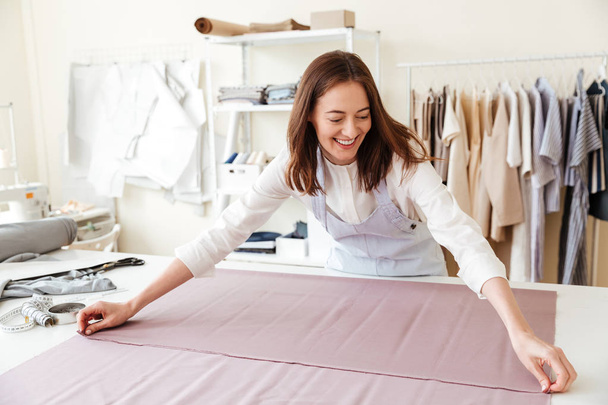 Woman seamstress spreading fabrics in workshop - Fotó, kép