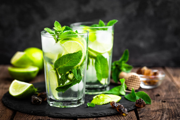 Refreshing mint cocktail mojito with rum and lime, cold drink or beverage with ice on black background - Фото, изображение