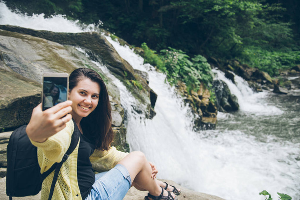vrouw nemen foto op de telefoon van de waterval op de achtergrond - Foto, afbeelding