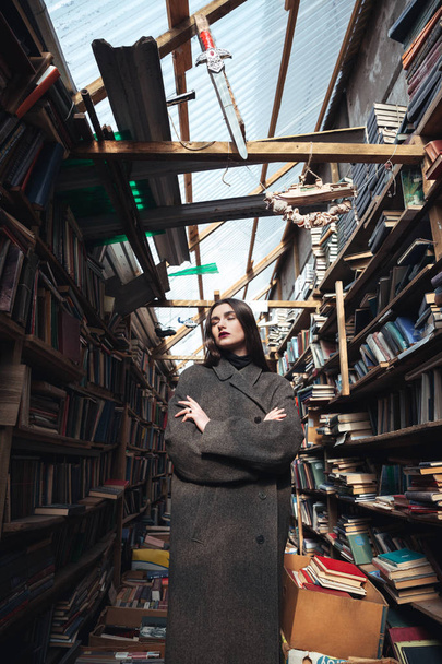 Young woman in coat standing in a book warehouse - Fotoğraf, Görsel