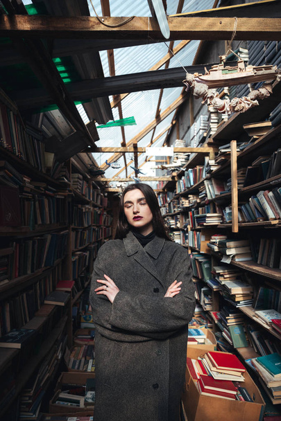 Young woman in coat standing in a book warehouse - Foto, afbeelding