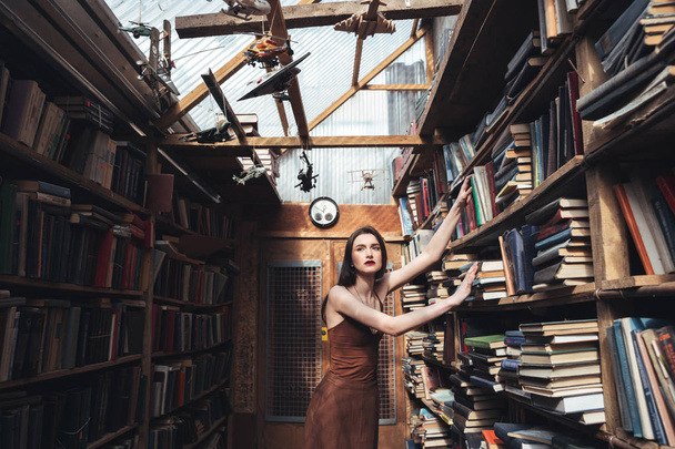 Young brunette girl standing among books - Foto, afbeelding