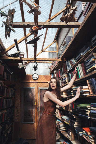 Young brunette girl standing among books - Valokuva, kuva