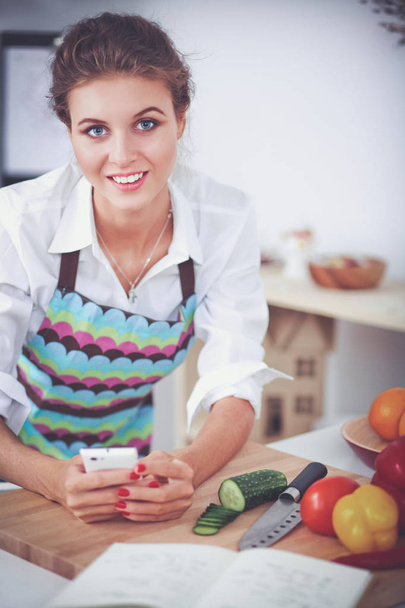 Smiling woman holding her cellphone in the kitchen - Foto, Imagen