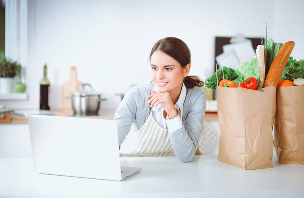 Smiling woman online shopping using computer and credit card in kitchen - Foto, Imagem