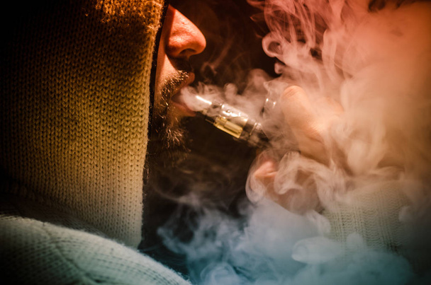 Vaping άνθρωπος που κρατά ένα mod. Ένα σύννεφο των ατμού. Μαύρο φόντο. Ηλεκτρονικό τσιγάρο με πολύ καπνό καπνίσματος - Φωτογραφία, εικόνα