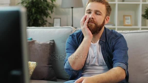 Attractive man with beard feeling borring and trying find some interesting film while sitting on sofa in the living room. - Кадры, видео