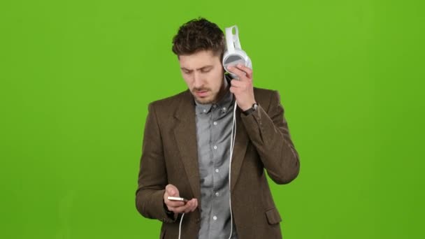 Businessman holds a phone and headphones, chooses music to listen to. Green screen - Video