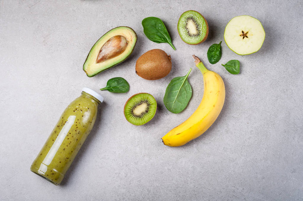 Healthy green smoothie and ingredients on gray background. Kiwi smoothie with fruits and vegetables. Superfoods, diet, detox, health, vegetarian food - 写真・画像