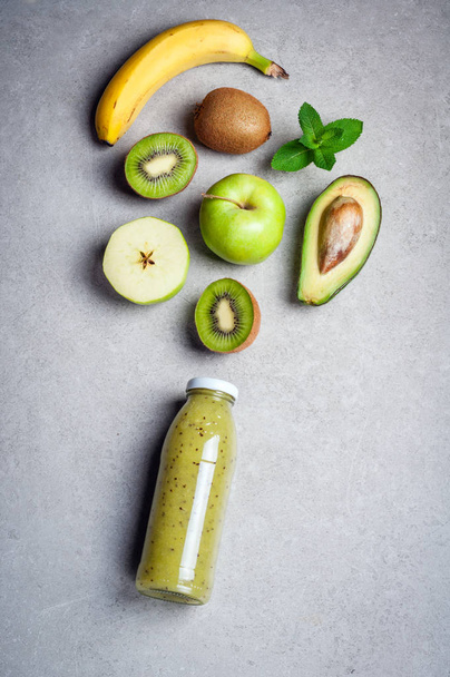 Healthy green smoothie and ingredients on grey background. Kiwi smoothie with fruits banana, avocado and apples. Superfoods, diet, detox, health, vegetarian food - Photo, Image