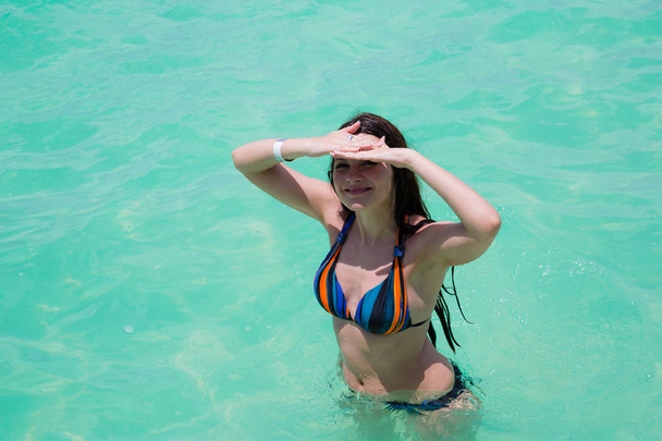 Gelukkige vrouw in zwembroek staat in water van de Oceaan kust tijdens vakantie zomertijd - Foto, afbeelding