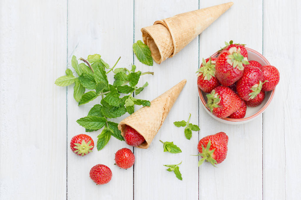 Bowl and cones filled with strawberries on a wooden table - Foto, Imagem