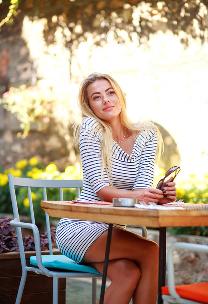 Young dreamy woman sits at table of summer cafe - Photo, Image