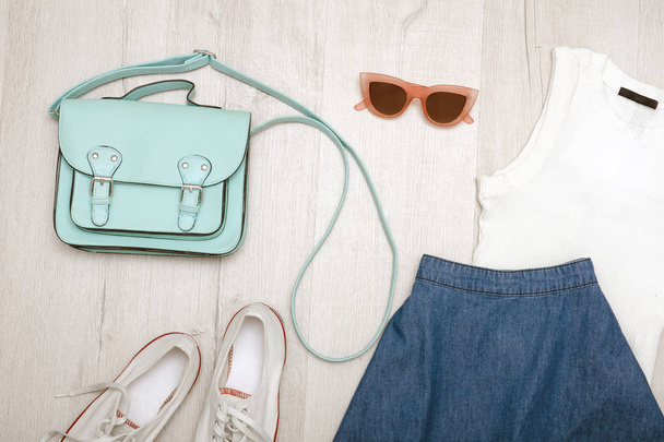 Jeans skirt, glasses, white shoes, white top and handbag. Fashionable concept. Wooden background. - Photo, Image