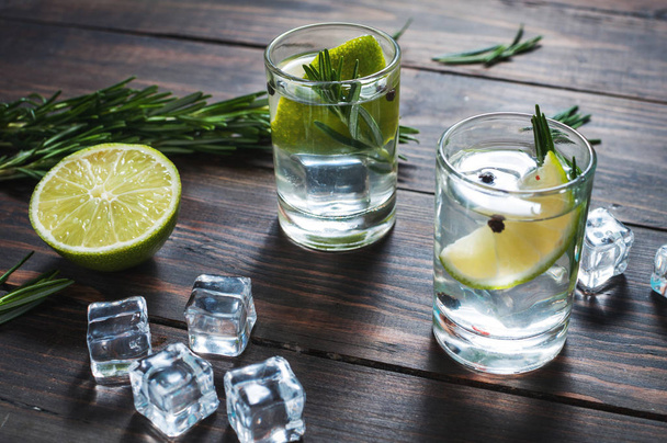 Boisson alcoolisée - cocktail gin tonic - avec citron vert, romarin et glace sur table rustique en bois
 - Photo, image