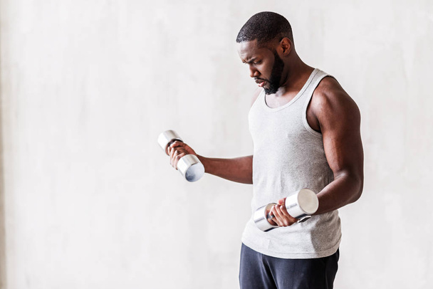 Strained bearded african sportsman doing exercises with hand weights - Φωτογραφία, εικόνα