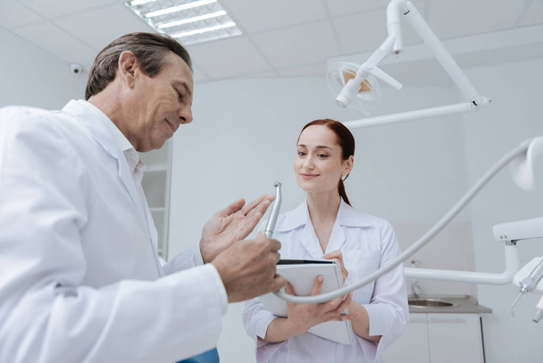 Profile photo of delighted dentist while showing instrument - Foto, imagen