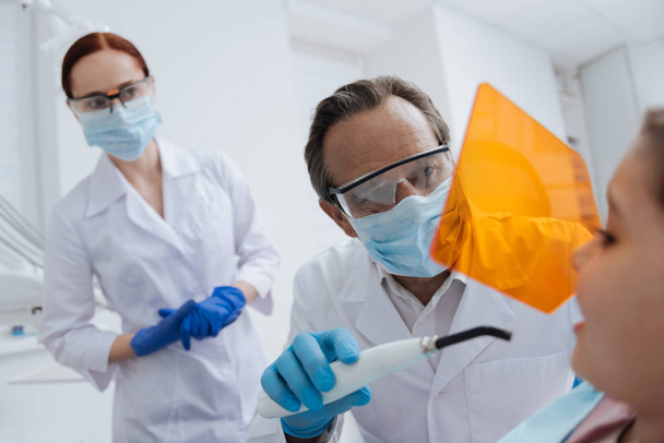 Estomatologista atento usando equipamentos especiais enquanto examina os dentes
 - Foto, Imagem