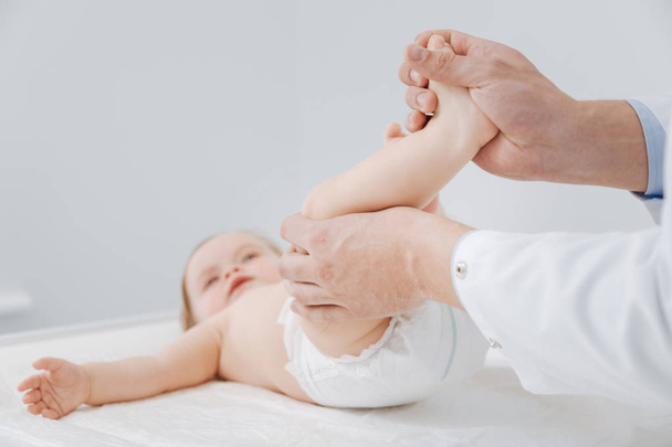 Neat professional pediatrician checking toddlers joints - 写真・画像