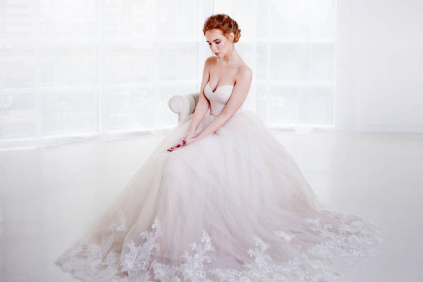 Portrait of a beautiful girl in a wedding dress. Bride in luxurious dress sitting on a chair - Фото, зображення