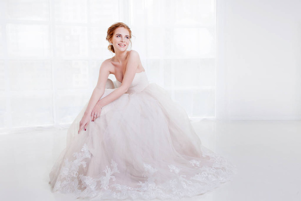 Portrait of a beautiful girl in a wedding dress. Sitting on the couch and laughs happily - Foto, Imagem