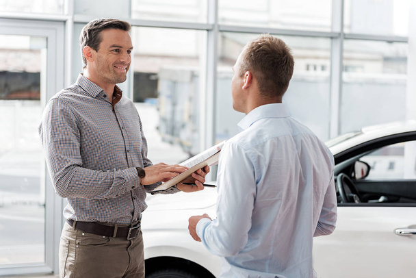Outgoing man telling with worker in car dealership - Foto, imagen
