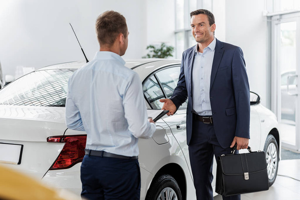 Cheerful male telling with consultant in car dealership - Foto, imagen
