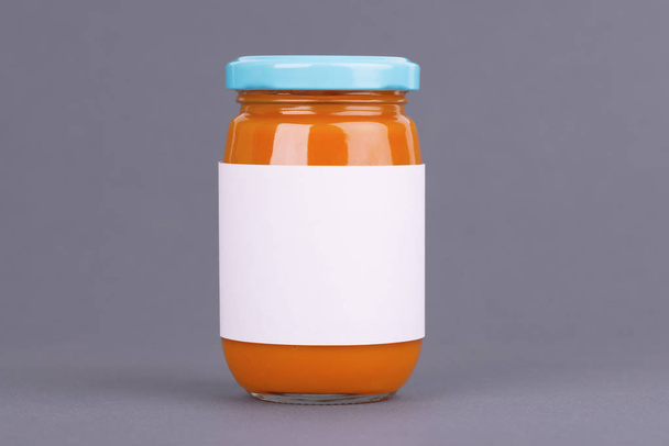 Narancssárga üvegedénybe baby élelmiszer-Bank a szürke háttér. Szerves baby élelmiszer püré. Mintája fel sablon design címke nélkül. - Fotó, kép
