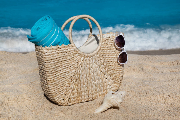 Saco de palha com toalha azul e óculos de sol na praia de areia tropical
 - Foto, Imagem