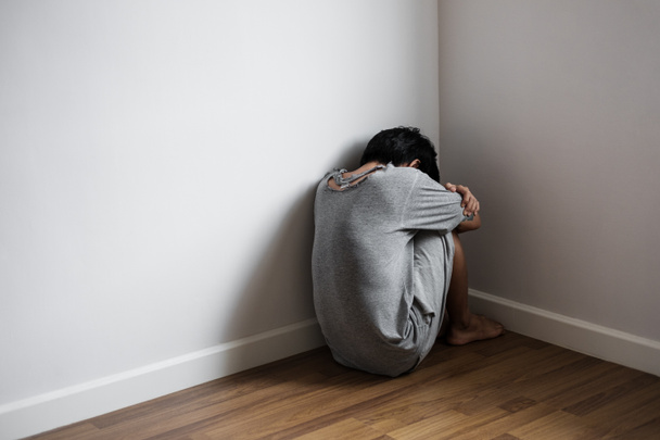 Μελαγχολικός νεαρός άνδρας κάθεται μόνος στη γωνία του δωματίου, θλίψη, κατάθλιψη, και της έννοιας προβλήματα ζωής - Φωτογραφία, εικόνα