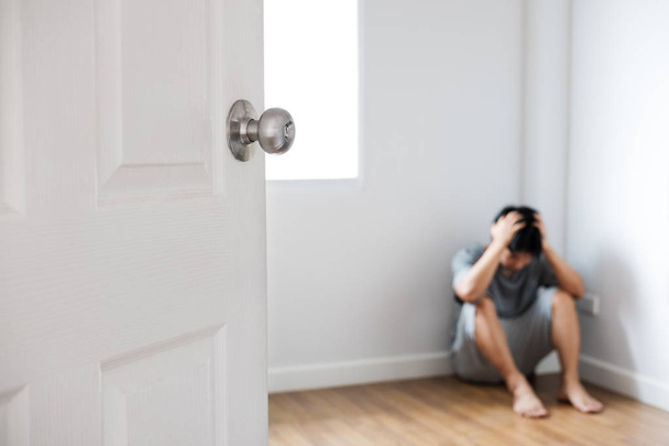 Drzwi otwarte z depresji facet siedzi w rogu pustym pokoju - Zdjęcie, obraz