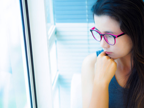 sad woman wear glasses sitting alone and looking through the window. - 写真・画像