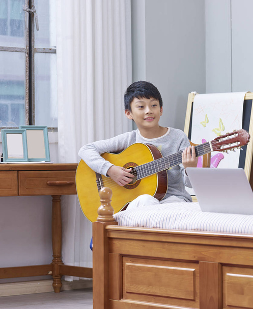 young asian boy practicing guitar at home  - Fotó, kép