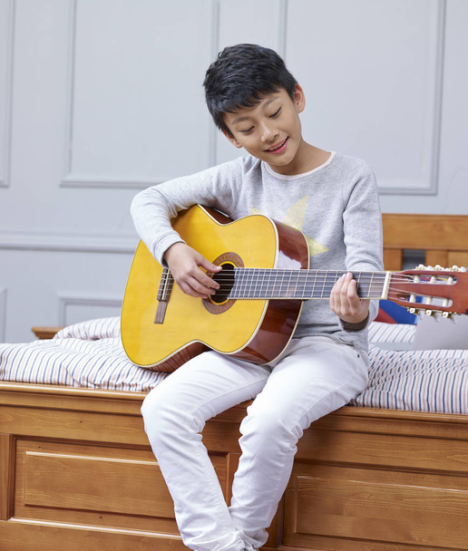 подросток азиатский мальчик играет на гитаре дома
 - Фото, изображение