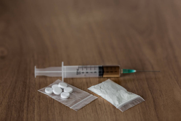 paquete de plástico con cocaína en polvo u otras drogas. jeringa sobre mesa de madera
. - Foto, Imagen