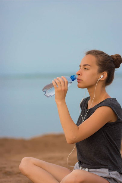 Selective focus Sports girl drinks water during a workout on the beach. The girl drinks water during fitness outdoors - Foto, Bild