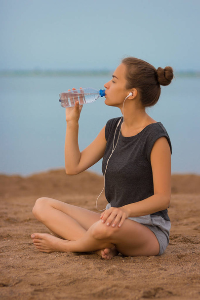 Selective focus Sports girl drinks water during a workout on the beach. The girl drinks water during fitness outdoors - Photo, Image