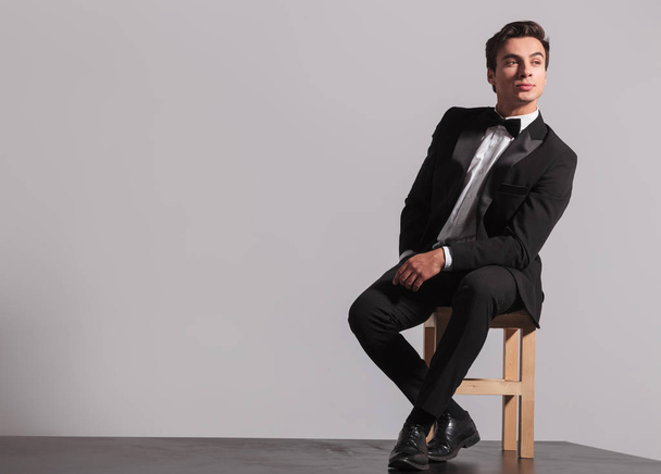 young model in tuxedo and bowtie sits on chair - Photo, Image