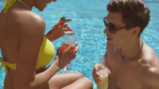 Young adult couple flirting and talking in the swimming pool and drinking cocktails, making cheers. Summertime pool party. Shot in 4k - 映像、動画