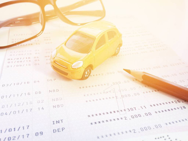 Μικρογραφία αυτοκίνητο μοντέλο, μολύβι, γυαλιά και λογαριασμός ταμιευτηρίου με βιβλιάριο ή οικονομική κατάσταση σε λευκό φόντο - Φωτογραφία, εικόνα
