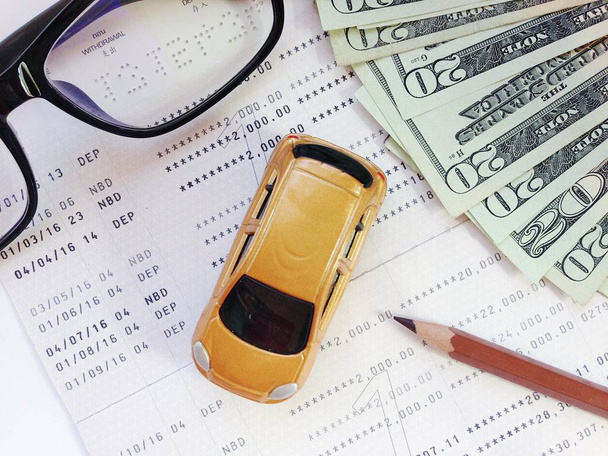 Modelo de carro em miniatura, lápis, óculos, caderneta de conta de dinheiro e poupança ou ficha financeira em fundo branco
 - Foto, Imagem