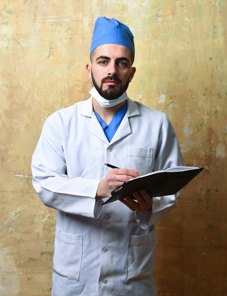 Surgeon with beard and tired face expression writes in notebook - Foto, afbeelding