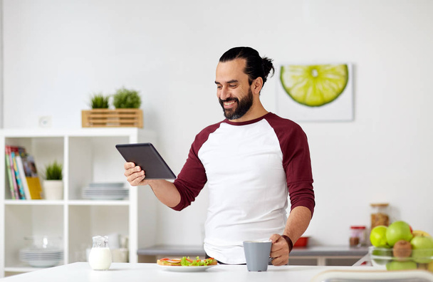 man with tablet pc eating at home kitchen - Fotografie, Obrázek