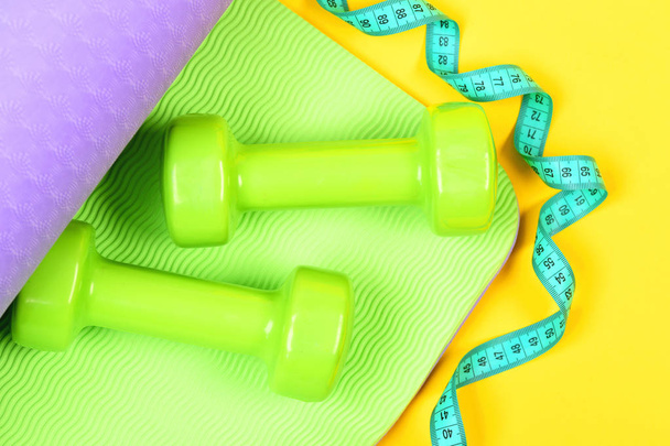 Measuring tape in cyan colour twisting around dumbbells and mat - Foto, immagini